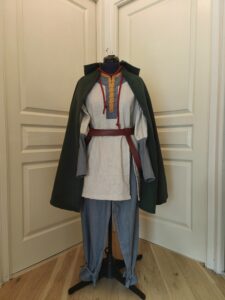 Costume de Olwyn du seigneur des anneaux. Pantalon en lin gris, tunique en lin beige avec détails gris et jaune. Ceinture en similicuir rouge Cape en lainage vert foncé