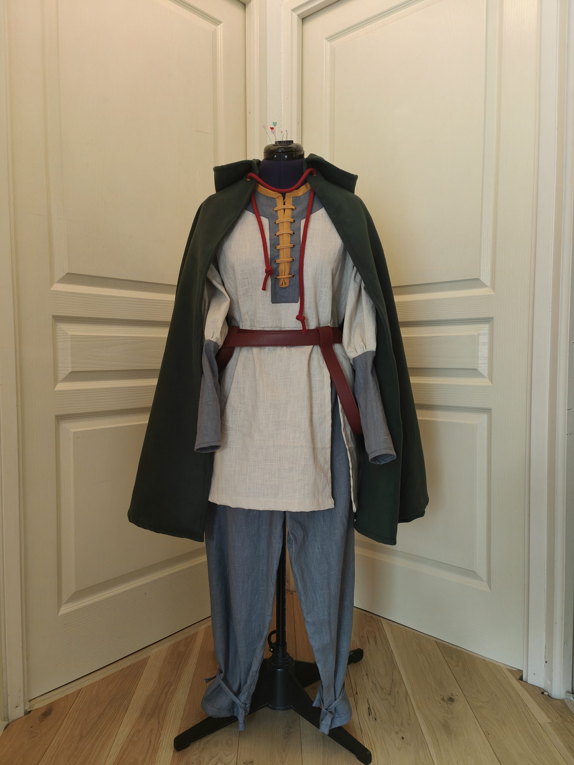 Costume de Olwyn du seigneur des anneaux. Pantalon en lin gris, tunique en lin beige avec détails gris et jaune. Ceinture en similicuir rouge Cape en lainage vert foncé